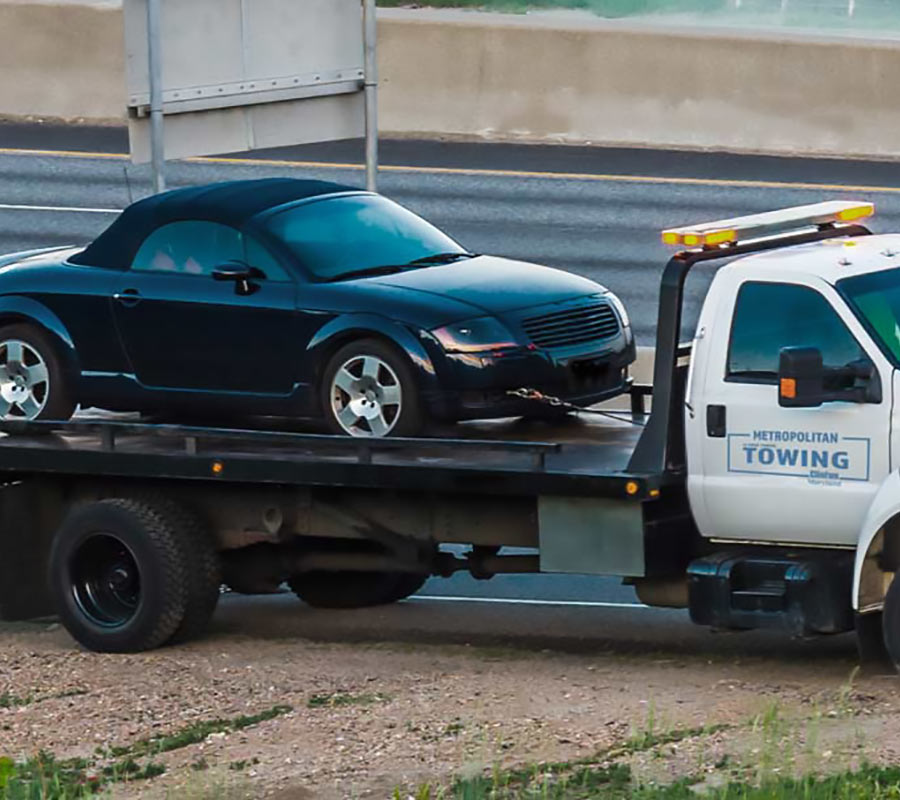 Metropolitan Towing flatbed truck transporting a car along the highway